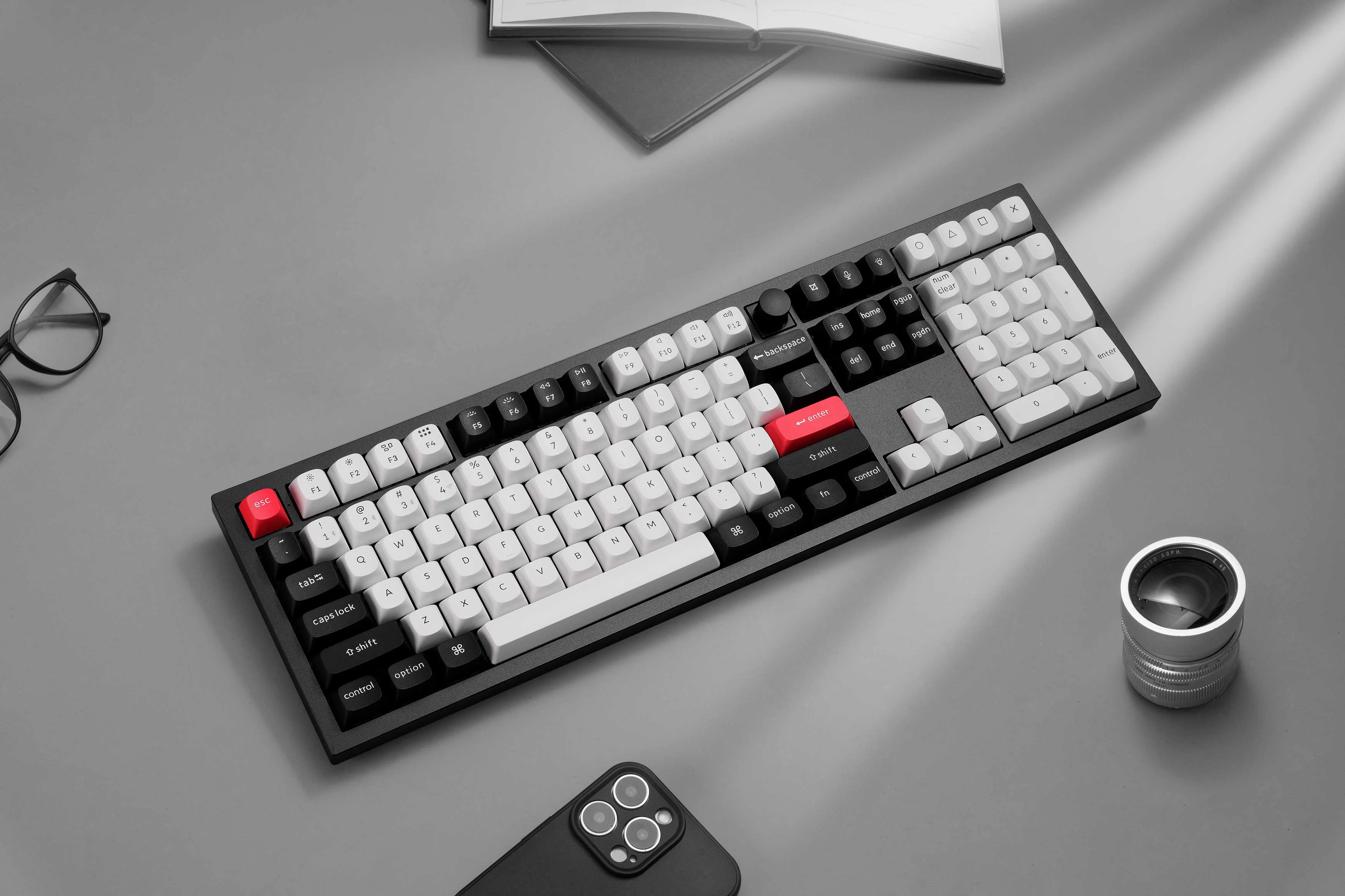 Keychron mechanisch full-size toetsenbord met zwarte en witte toetsen en rode accenten op een bureau met bril en smartphone