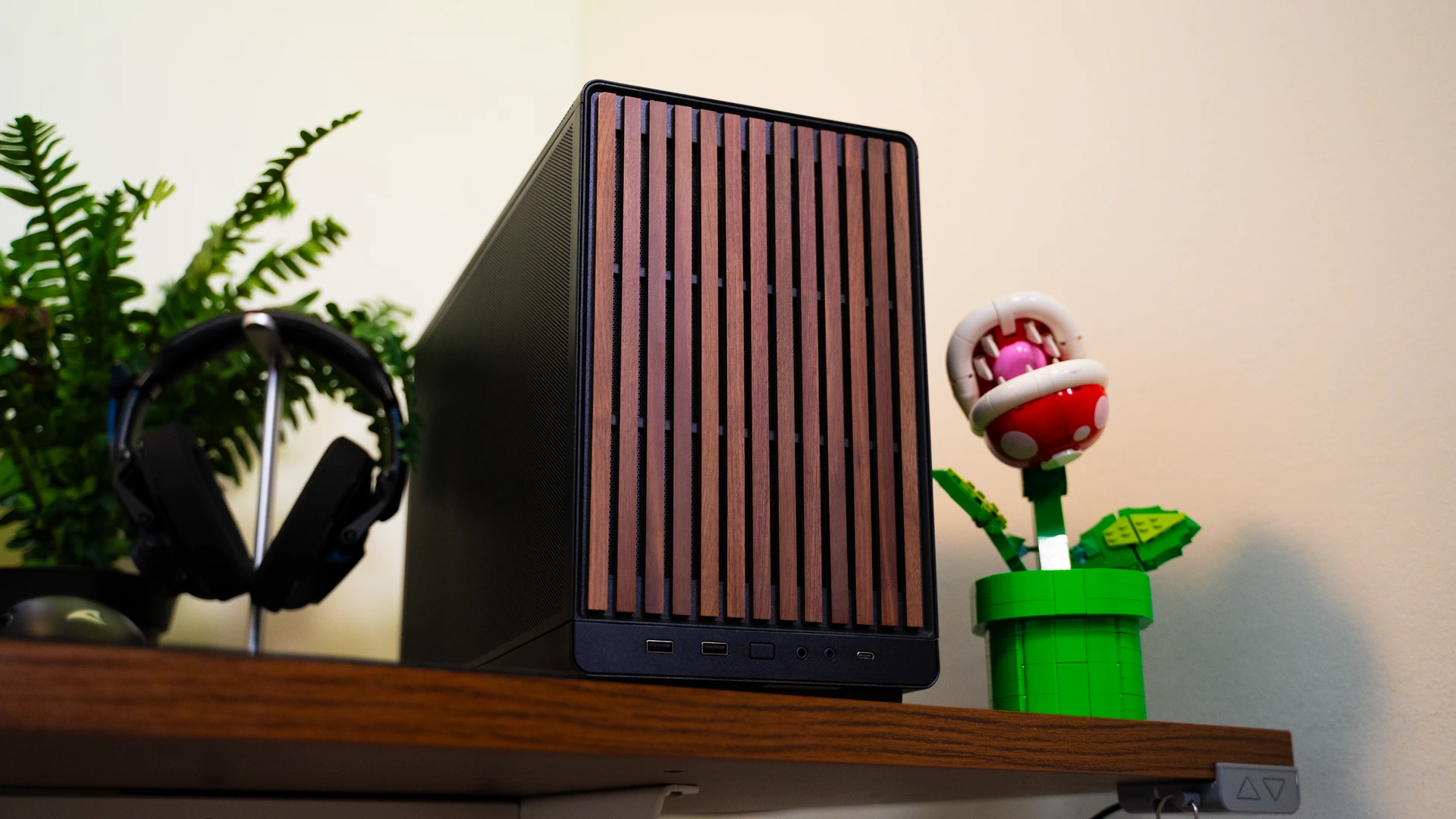 Compacte zwarte pc met houten frontpaneel naast gaming monitor