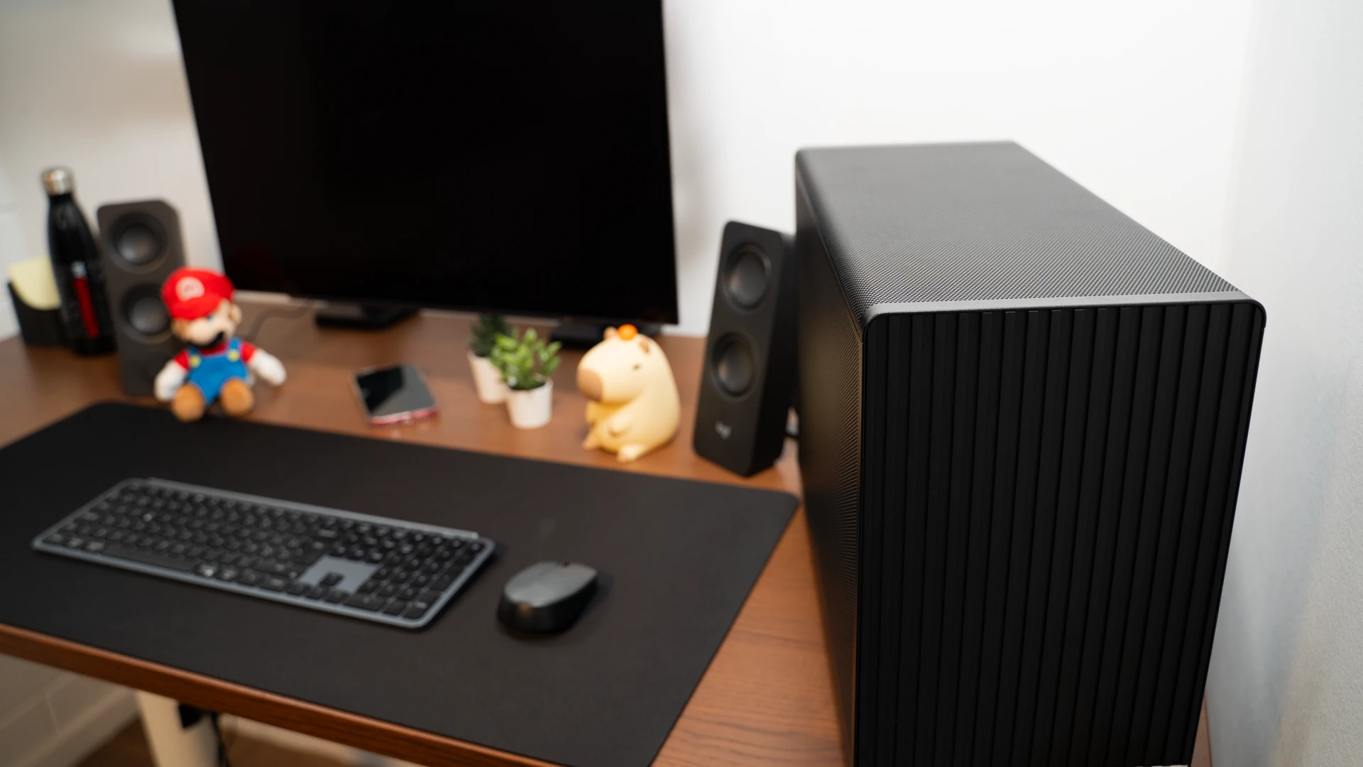 Compacte zwarte pc met houten frontpaneel naast gaming monitor