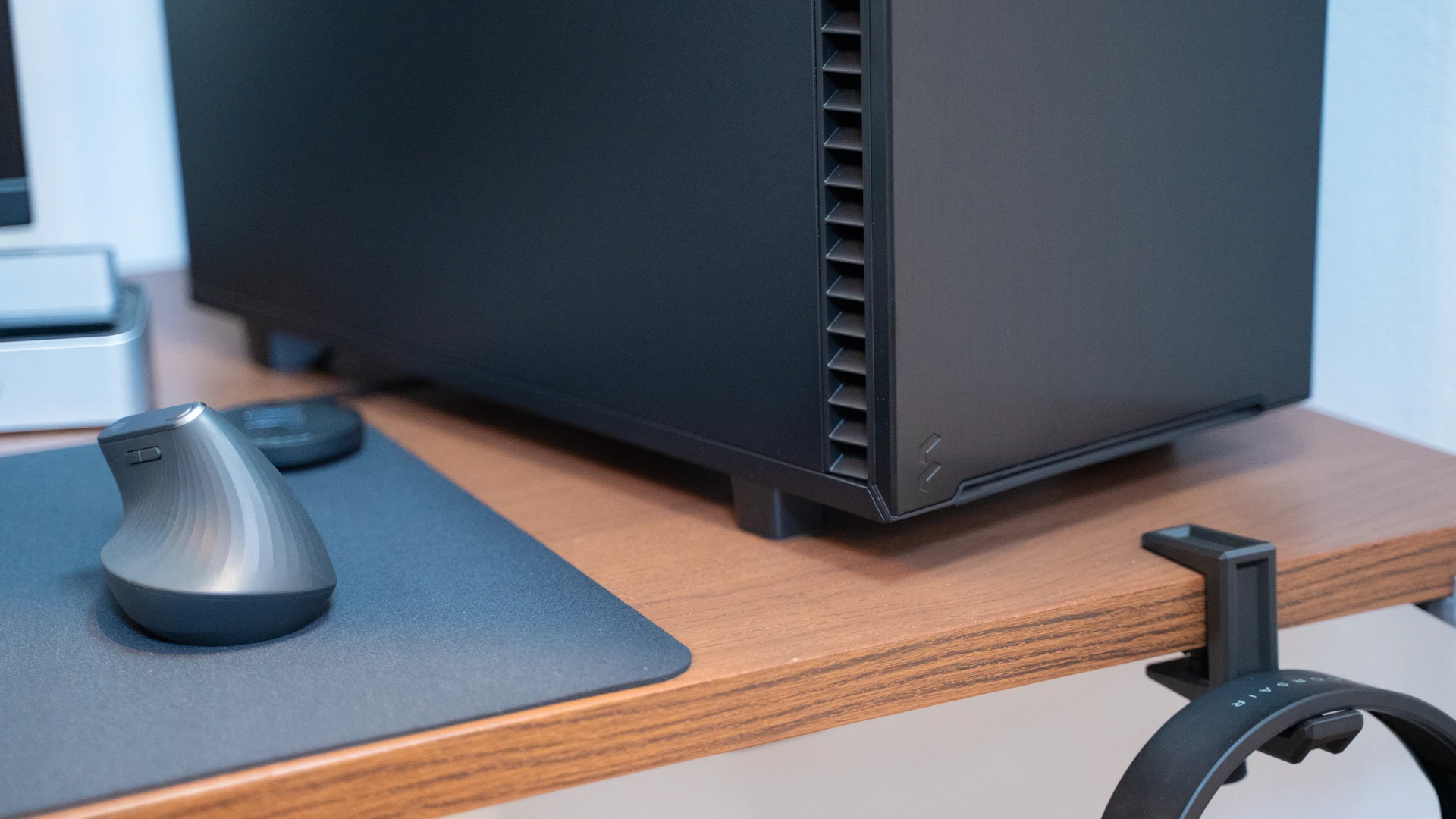 Compacte zwarte pc met houten frontpaneel naast gaming monitor